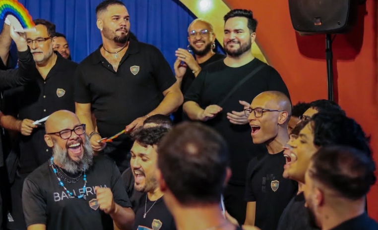 Integrantes do CHGSP cantando juntos, com leques coloridos ao fundo